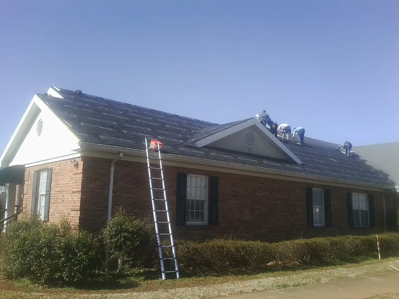 Crew tearing shingles off a brick ranch roof with a ladder set — Emergency Roof Repair work by our crew in Noxen