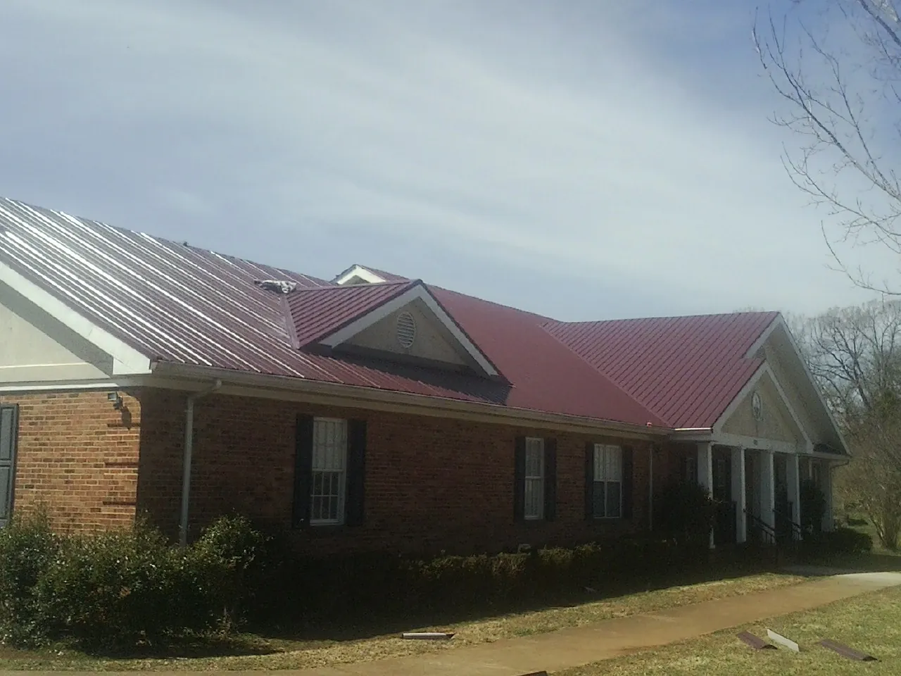 Red metal roof with gabled entries on a long brick building, from a Hail Damage Roof Repair job in Noxen