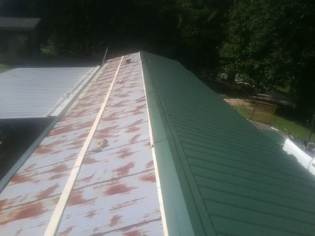 Old rusted panels beside newly installed green metal roofing — Wind Damage Roof Repair by Roofing Brothers in Noxen