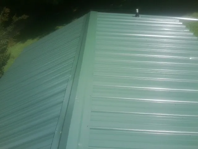 New green metal panels meeting at the ridge of a roof — Flat Roof Repair work by our crew in Noxen