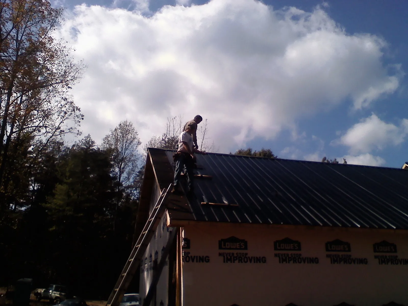 Roofer fastening dark metal panels high against a cloudy sky, from a Roof Inspection job in Noxen