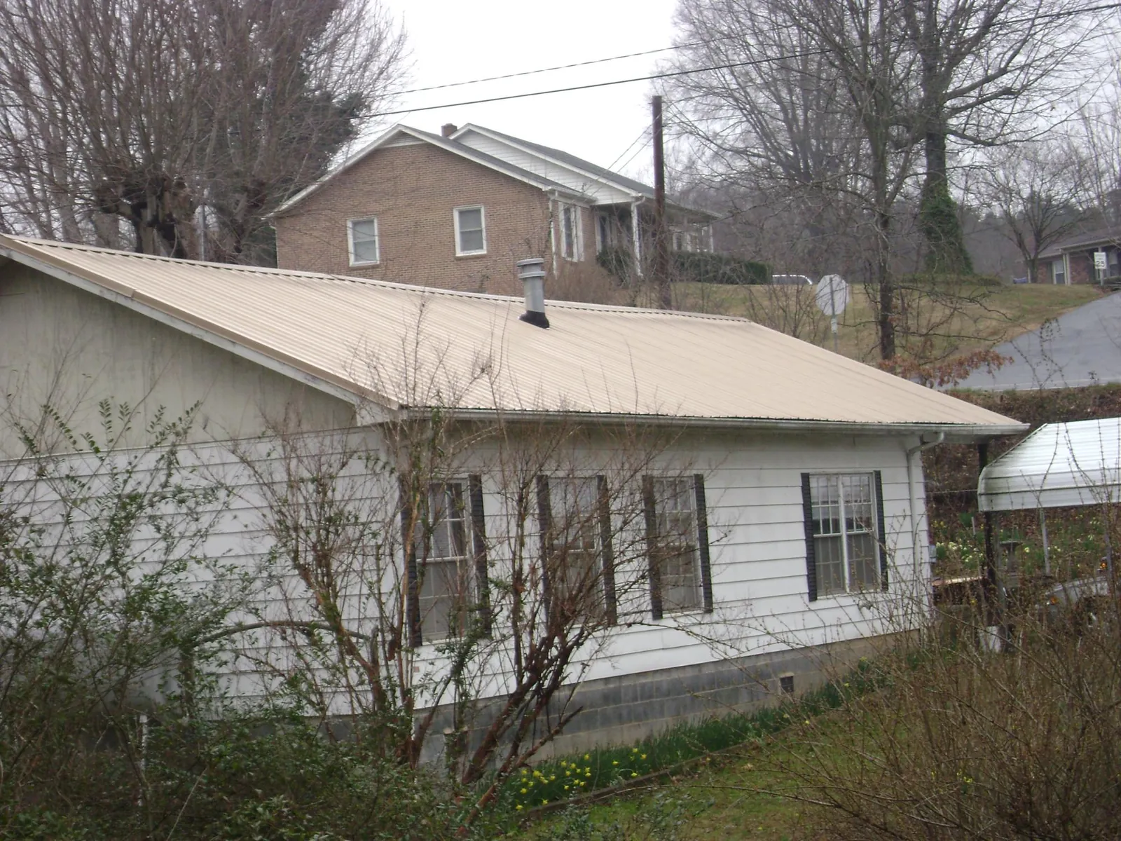 Tan metal roof on a white sided house set into a hillside — Commercial Roofing by Roofing Brothers in Noxen